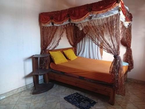 a bedroom with a canopy bed with yellow pillows at TAMATAVE Chez Bien Aimée in Toamasina