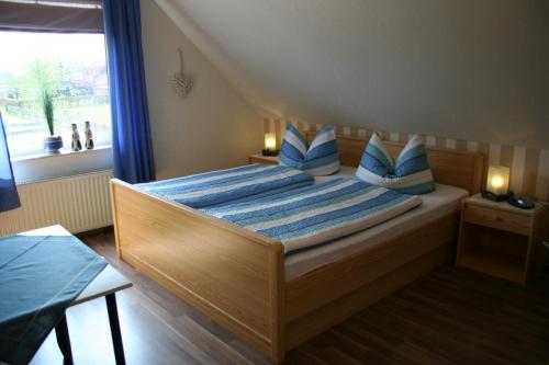 sypialnia z łóżkiem z niebieskimi poduszkami i oknem w obiekcie Landgasthaus Fecht w mieście Aurich