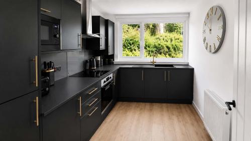 a kitchen with black cabinets and a clock on the wall at Bayview at the Port in Port Bannatyne