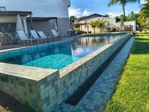 a swimming pool with a tiled retaining wall next to a house at Pé na areia, 3 suítes, terraço com piscina privativa in Camacari