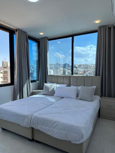 a bedroom with a large bed with large windows at Amman Suites in Amman