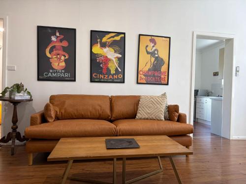 a living room with a brown couch and four posters at Mary Lemon Cottage - Heritage Home in Orange
