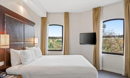 a hotel room with a bed and two windows at Amora Herencia Riverwalk Melbourne in Melbourne