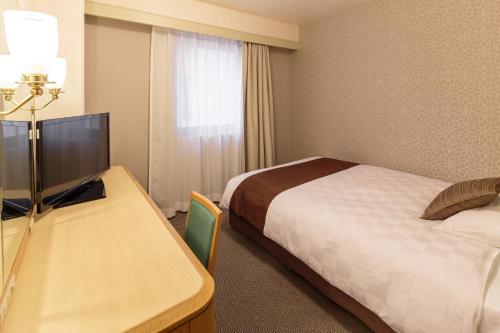 a hotel room with a bed and a desk with a television at Matsuyama Tokyu REI Hotel in Matsuyama