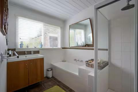 a bathroom with a tub and a sink and a mirror at Clambake Beach House in Cape Woolamai