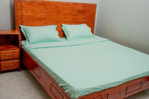a bed with a wooden headboard and blue pillows at Kasese Explorers Homestay in Kasese