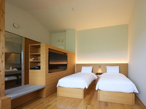 two beds in a room with a tv and a bed sqor at 友愛ファームゲストハウス in Hatoyama