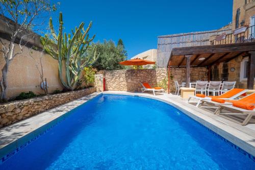 a swimming pool with orange chairs and a house at Il-Mohba Holiday Home in Munxar