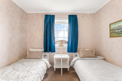 two beds in a room with blue curtains and a window at Reine Panorama in Reine