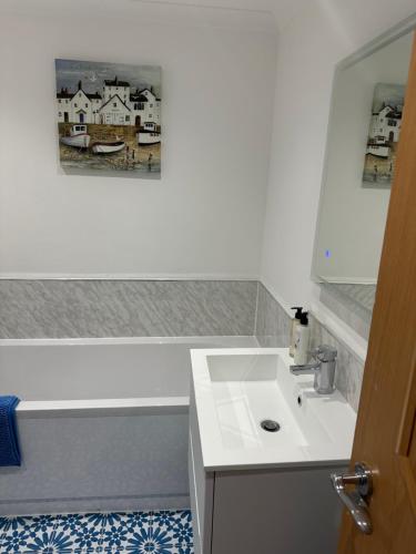 a white bathroom with a sink and a picture on the wall at Waters Reach in Abersoch