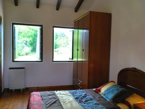 a bedroom with a bed and a cabinet and two windows at Cuetu del Pradón in Piñeres