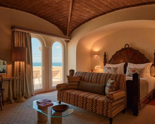 a bedroom with a bed and a couch and a table at Hotel Fortaleza do Guincho Relais & Châteaux in Cascais