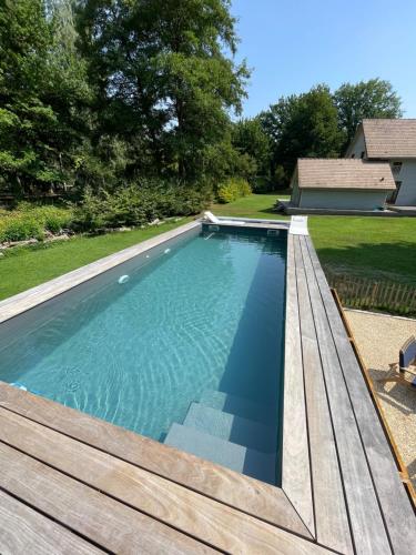 a swimming pool with a wooden deck next to a house at Ecrin de Vizaille in Toucy