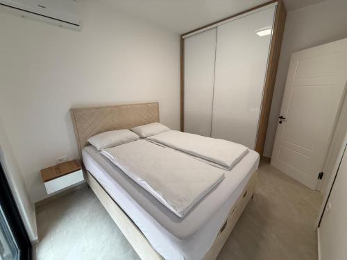 a bedroom with a bed with white sheets and a door at Sea Sand Apartment in Bijela Glavica