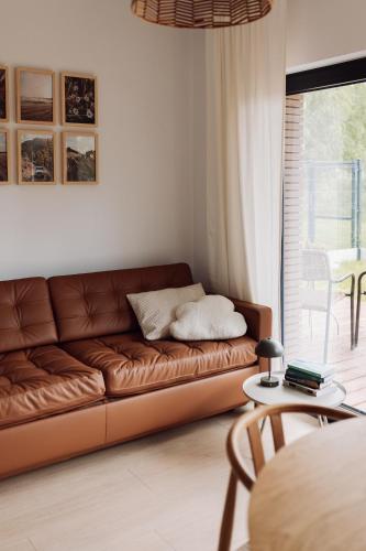 a brown leather couch in a living room with a table at Apartamenty Wrzosowa 23 z garażem na rowery in Kudowa-Zdrój
