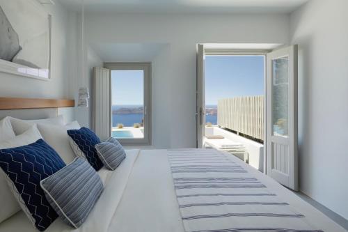 a bedroom with a large white bed with blue pillows at Grace Hotel, Auberge Collection in Imerovigli