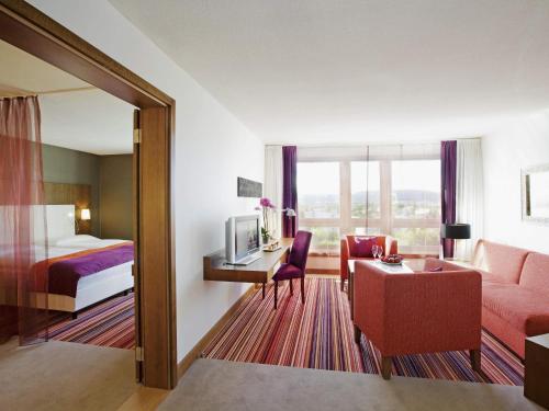 a hotel room with a bed and a living room at Mövenpick Hotel Zurich Airport in Glattbrugg