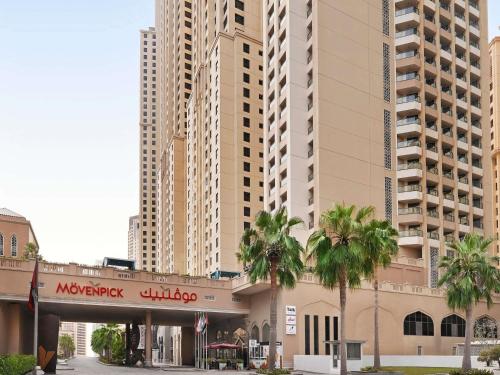 a building with palm trees in front of tall buildings at Mövenpick Hotel Jumeirah Beach in Dubai