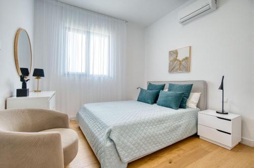 a white bedroom with a bed and a chair at Modern Sea-View Work Apartment, Sit-Stand Desk, Pool, Gym & Walk to Old Town in Paphos