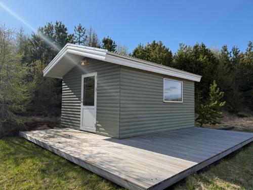 a small shed with a wooden deck in the grass at Lífsbót - riverside cottage in Egilsstaðir