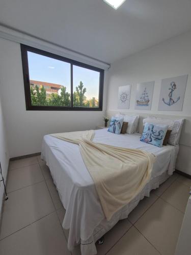 a white bedroom with a large bed with a window at Aconchegante Flat em condomínio na beira mar de Muro Alto - Malawi Beach Resort in Porto De Galinhas