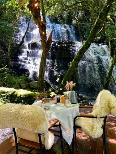 a table and chairs with a table and a waterfall at Lumine Cabanas- Chalé na Serra Gaúcha in Farroupilha