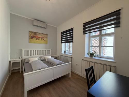 a bed in a room with a table and two windows at Zwinger Apartman in Sopron