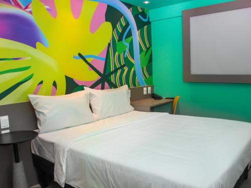 a bedroom with a white bed with a painting on the wall at Ibis Styles Garanhuns in Garanhuns