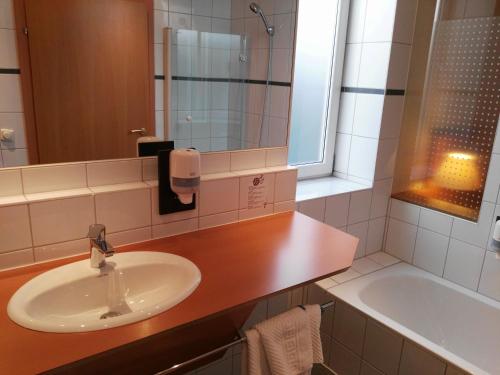 ein Badezimmer mit einem Waschbecken, einem Spiegel und einer Badewanne in der Unterkunft Hotel Wirt im Feld in Steyr