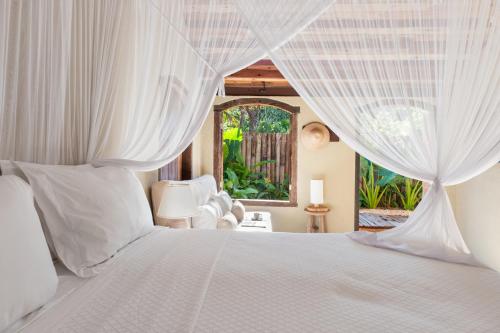a bedroom with a white bed with a window at Casa do Amor Caraíva in Caraíva