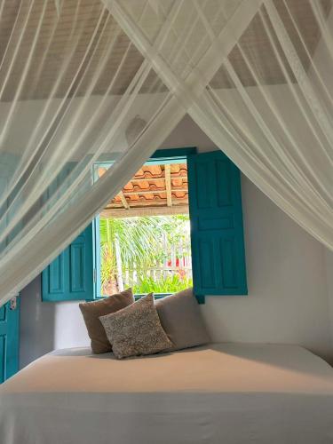 a white bed with blue shutters and a window at OCA Caraíva in Caraíva