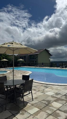 a table with an umbrella next to a swimming pool at Flat em Gravatá - Villa Monte Castelo in Sairé