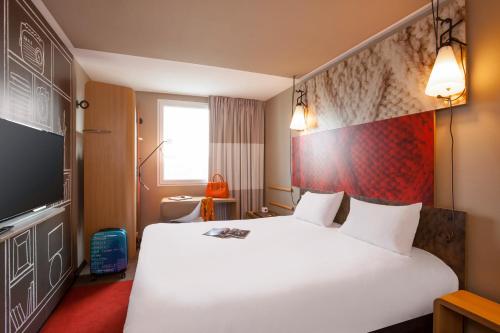 a hotel room with a large white bed and a tv at ibis Honfleur in Honfleur