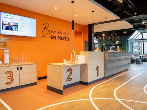 a restaurant with an orange wall and a counter with numbers on it at ibis Styles Colombes Paris Ouest (Ouverture Octobre 2025) in Colombes