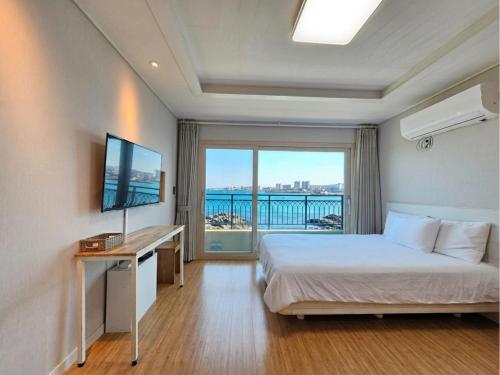 a bedroom with a bed and a desk and a window at Haemorat Pension in Seogwipo