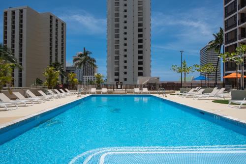 a large swimming pool with lounge chairs and buildings at Waikiki condo - ocean views, lanai & beach access in Honolulu