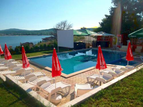 a swimming pool with chairs and red umbrellas at Safo Apartments and Rooms in Sozopol