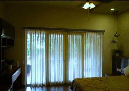 a bedroom with a bed and a large window with curtains at Mannath Lake House in Murinjupuzha