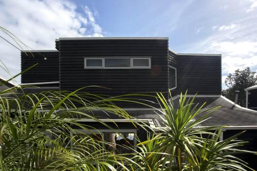 a black house with plants in front of it at Chester Cottage Beachfront - direct ocean access in Oakura