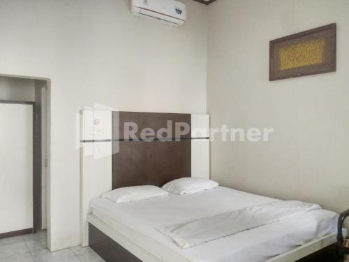 a white bedroom with a bed with a wooden headboard at The SO Hotel Mitra RedDoorz in Pangandaran