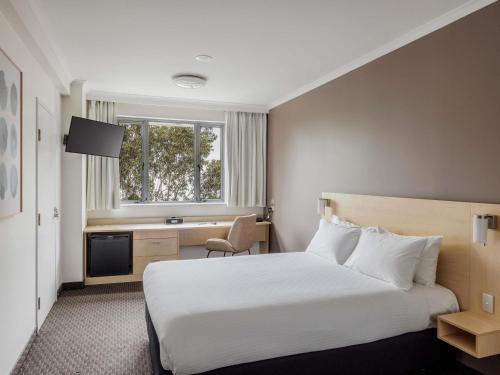 a hotel room with a bed and a desk and a window at ibis Sydney Olympic Park in Sydney