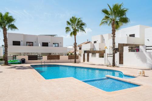 a swimming pool in front of a building with palm trees at Bungalow Fausto Sunrise in Orihuela Costa