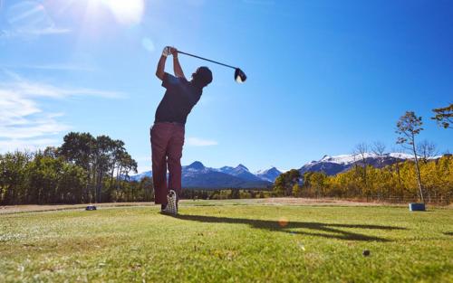 a man swinging a golf club in a field at Glacier Park Lodge in East Glacier Park