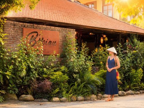a woman in a hat standing in front of a building at B'Hoian Retreat in Hoi An
