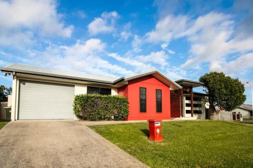 a house with a red house in the grass at WhitsunStays - Casa Crimson in Mackay