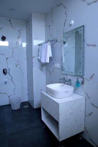 a white bathroom with a sink and a mirror at Hotel Maurya Greens in Banbāsa
