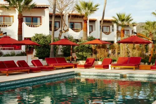 a hotel with red chairs and umbrellas next to a swimming pool at Petunia Ibiza, a Beaumier hotel in Cala Vadella