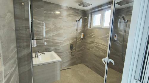 a bathroom with a shower and a sink and a glass shower door at Къща за гости Орфей in Dospat