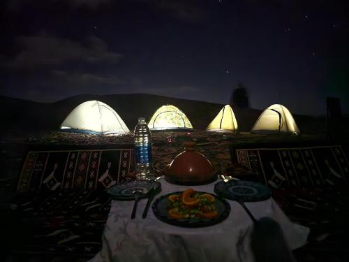 a table with a meal in front of tents at night at Desert mountains camping in Merzouga