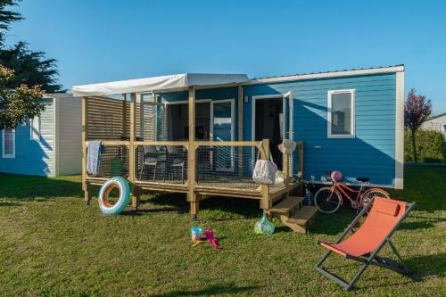 a blue tiny house with a porch and a chair at Camping 3 étoiles - Piscine - ccbffbc in Saint-Denis-dʼOléron